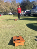 Young kid outside playing the cornhole game on grass.