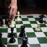 Person playing a game of chess with triple weighted Staunton chessmen, black and cream.