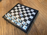 Magnetic board with chess and checker pieces and dice in the middle of board.