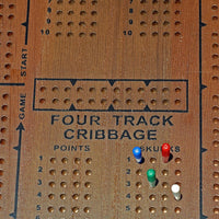 Zoomed in on center of board. Reads Four Track Cribbage. 4 colored pegs in board.